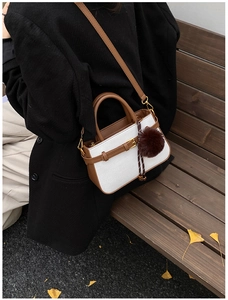 Detail of white woven bucket bag with brown leather trim and cute pompom charm