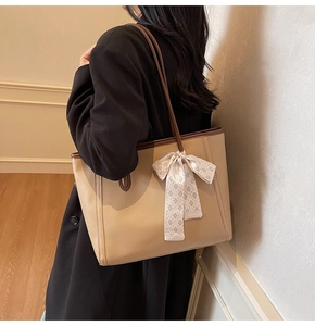 Detail of khaki tote bag with brown leather trim and silk scarf styled on shoulder