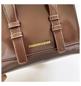 Detail of dark brown patent leather bag with gold FASHION & BAGS logo and strap buckles