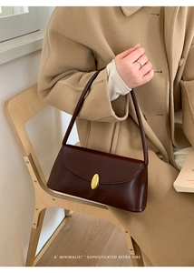 Close-up of a retro brown leather baguette bag featuring a gold oval buckle detail