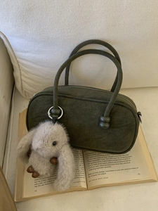 Olive green bowling handbag with plush rabbit charm on a minimalist book display