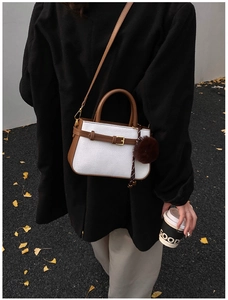 Detail view of woven bucket bag with brown leather trim and plush pom-pom charm