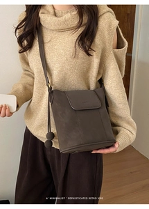 Détail du sac seau en daim marron foncé avec deux breloques sphériques sur la bandoulière