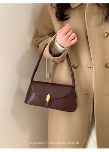 Detail of a dark brown leather baguette bag with a golden oval metal buckle on a shoulder strap