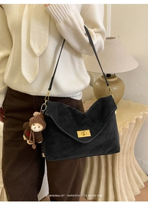 Close-up of black suede shoulder bag with contrast stitching and golden square lock