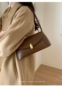 Close-up of a brown leather shoulder bag with a gold buckle on a camel wool coat