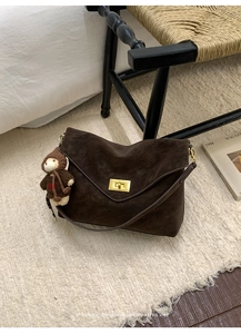 Detail of dark brown suede shoulder bag with gold metal clasp and cute bear charm pendant