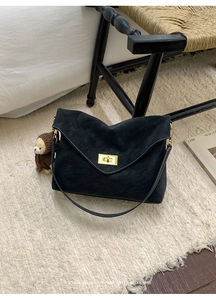 Detail of black suede shoulder bag with contrast stitching and golden turn-lock closure