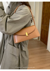 Close-up of caramel leather baguette bag with golden buckle on olive trench coat