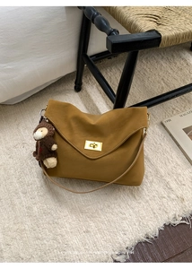 Detail of ginger yellow shoulder bag with gold clasp and plush bear charm on soft rug