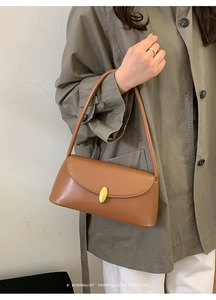 Brown leather baguette bag with gold oval buckle shown on a model in khaki coat