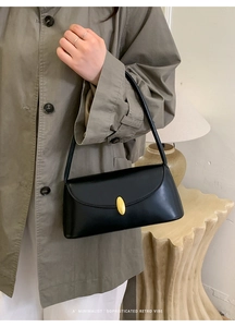 Detail of black minimalist leather underarm bag with gold oval buckle on a model