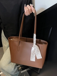 Minimalist large brown leather tote bag with plaid scarf on shoulder of a model