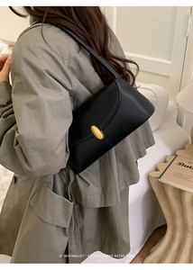 Detail of a black minimalist leather shoulder bag with a textured gold oval metal clasp