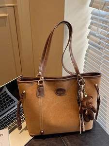 Brown faux suede tote bag with contrast stitching and teddy bear charm in office setting