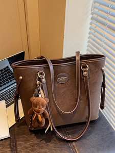 Brown textured leather tote bag with bear charm and tassel detail in a workspace setting