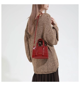 Detail of red leather mini bag with gold hardware worn over a brown knit sweater
