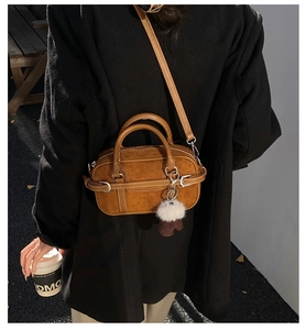 Détail d'un sac bowling en daim marron avec charms porté sur un manteau noir élégant
