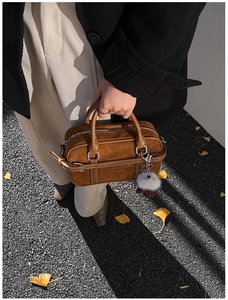 Détail du sac bowling en daim marron avec surpiqûres et breloque sur une rue d'automne