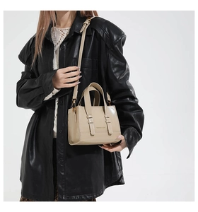Detailed view of cream-colored small square bag with metal buckle straps and top handle