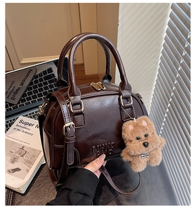 Detail of dark brown glossy Boston bag with bear charm on desk with laptop and books