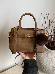 Retro brown woven bucket bag with pom-pom charm and top handle on a minimalist background
