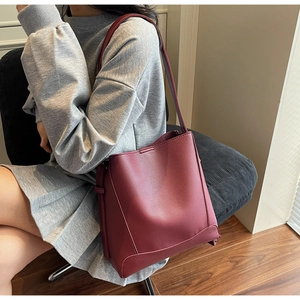 Detail view of burgundy pebble leather bucket bag worn by model on a shoulder