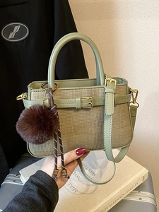 Light green retro bucket bag with leather trim and plush pom-pom charm on black blazer