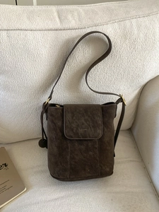 Sac seau minimaliste en daim marron foncé avec bandoulière sur un canapé crème