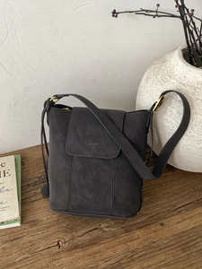 Sac seau gris foncé en cuir mat avec breloques à cordon sur un support en bois