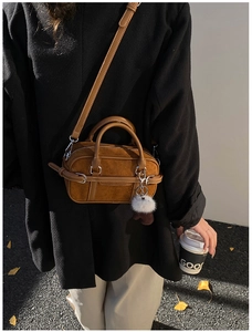 Brown suede bowling bag featuring long strap and plush ball charm in outdoor setting