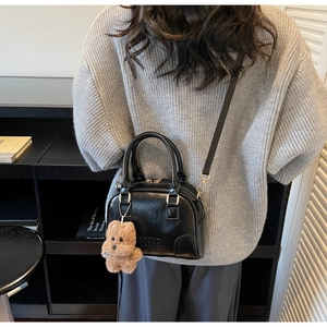 Detail of black faux leather Boston bag with teddy bear charm and adjustable shoulder strap