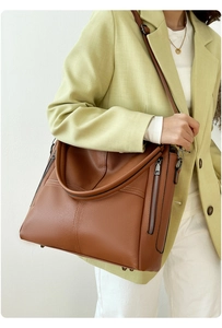 Close-up of a brown leather tote bag showing side zippers and fine pebble texture details