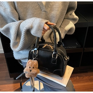 Detail of black leather Boston bag featuring gold zippers and a plush bear pendant