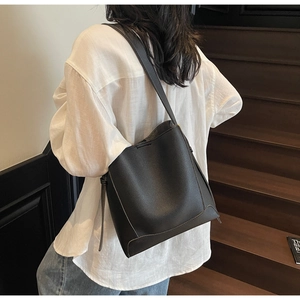 Detail of black lychee-grain leather bucket bag with long strap shown in a lifestyle scene