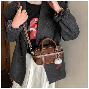 Deep brown suede mini bag with white stitching shown on a model in a grey blazer
