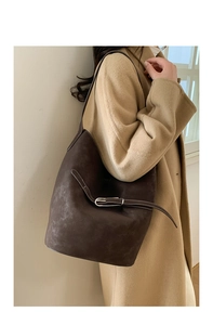Détail d'un grand sac seau en daim marron foncé porté avec un manteau en cachemire beige