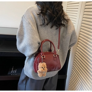 Detail of burgundy glossy leather Boston bag with plush dog charm on a shoulder strap
