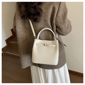 Detail of a creamy white pebbled leather bucket bag with metallic twist lock on shoulder