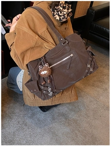 Detail of dark brown suede tote bag with silver zippers and plush ball charm on a model