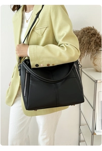 Detail of black pebbled leather tote bag with side zippers and protective base studs