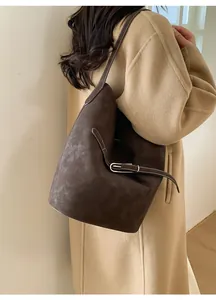 Détail d'un sac seau marron foncé avec boucle argentée ajustable sur un manteau camel