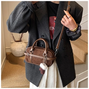 Close-up of brown suede bowling bag with metal ring handles and plush glove charm decoration