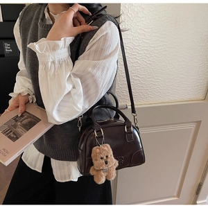 Detail of dark brown glossy patent leather Boston bag with a cute plush bear charm