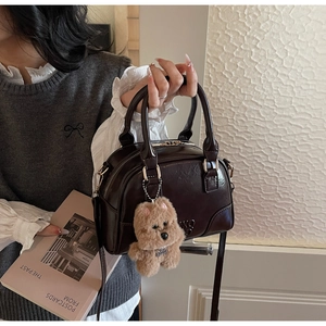 Detail of dark brown patent leather bowling bag with plush dog charm and dual handles