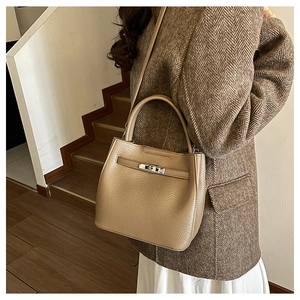 Detail view of tan lychee grain leather bucket bag with metal twist lock on a model