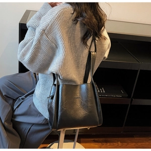 Detailansicht der schwarzen Leder-Beuteltasche, getragen von einem Modell in Innenräumen