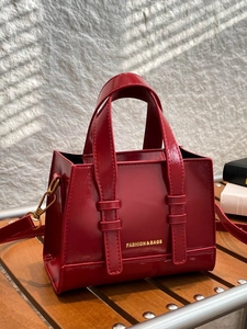 Glossy red faux leather satchel bag with top handles on wooden table in natural light