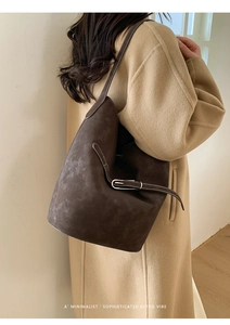 Détail d'un sac seau marron foncé avec texture mate et boucle en métal argenté sur modèle