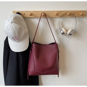 Detail showing high-quality burgundy leather bucket bag hanging on a wooden wall hook